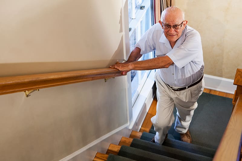 senior man holding handrail going up stairs